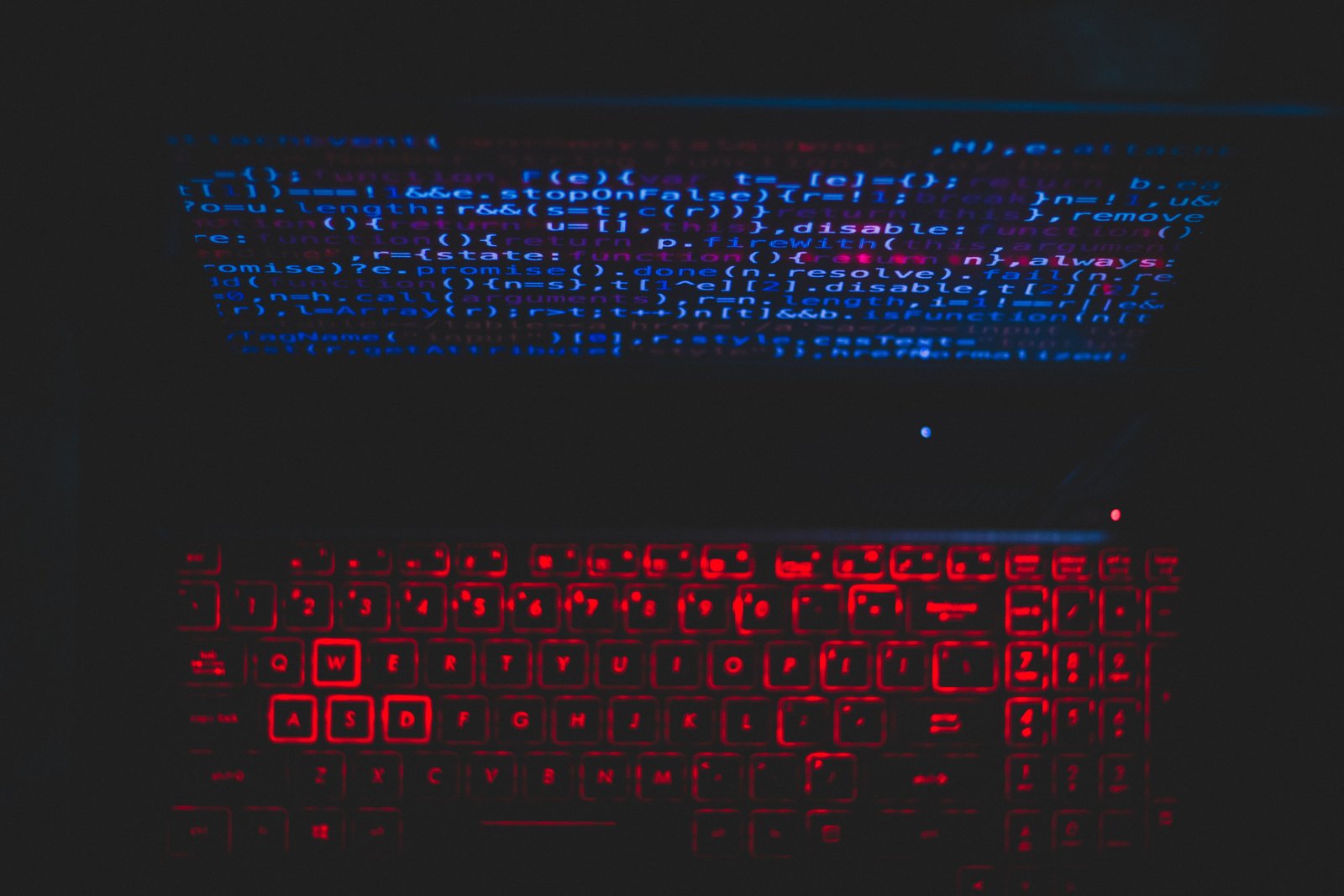 Laptop mit Quellcode und rot beleuchteter Tastatur
